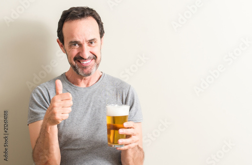 Senior man drinking beer happy with big smile doing ok sign, thumb up with fingers, excellent sign