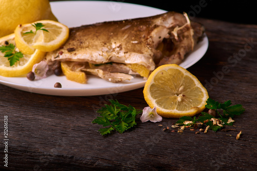 On a wooden table plate with roasted carp fish dorado with parsley, chives and lemon. Concept health food