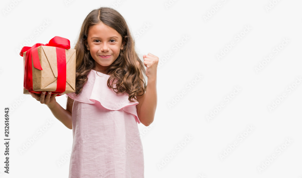 Brunette hispanic girl holding a gift screaming proud and celebrating victory and success very excited, cheering emotion Brunette hispanic girl holding a gift screaming proud and celebrating victory and success very excited, cheering emotion