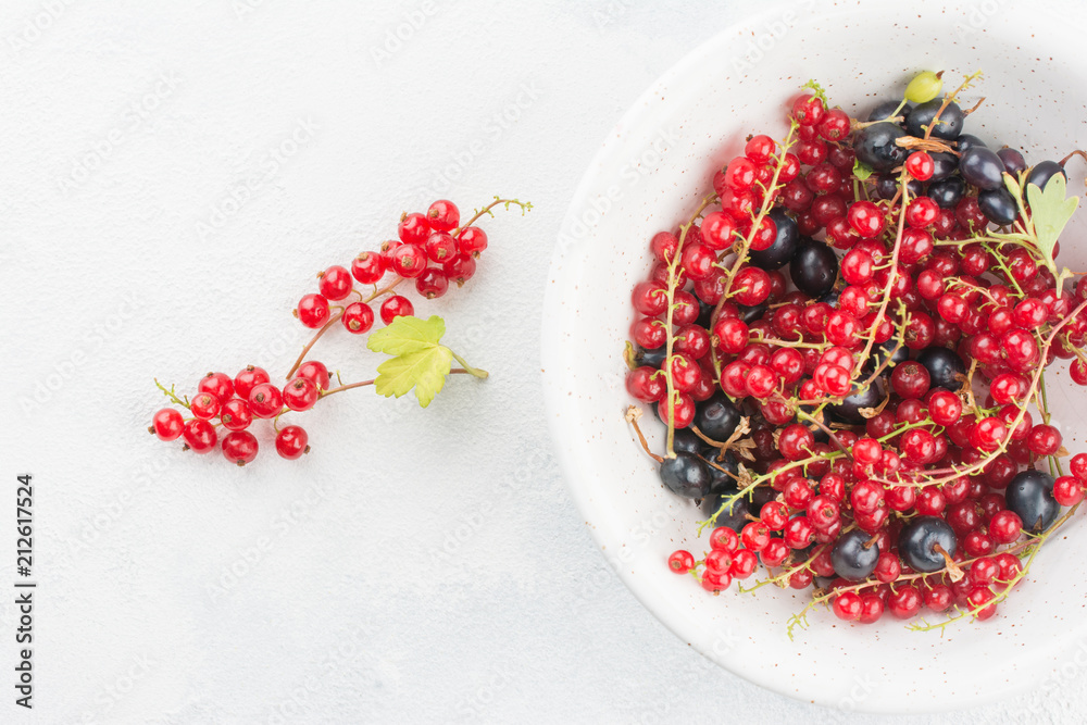 Close up top view of white cup with red and black currant berry and small bunch of red currant with green leaf of currant bush in left of cup on white concrete background. Summer concept copyspace Close up top view of white cup with red and black currant berry and small bunch of red currant with green leaf of currant bush in left of cup on white concrete background. Summer concept copyspace