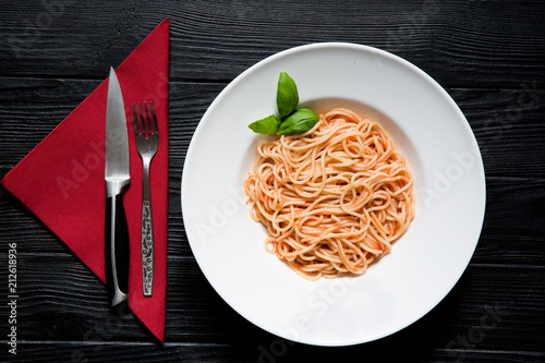 Vegetarian spaghetti with tomato, basil and cheese parmesane on black wooden background, served with fork and napkin on red velvet napkin, top view. Meditteranean diet. photo