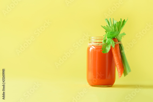 Fresh carrot juice with carrots, celery on yellow background. Vegetable smothie in glass jar. Copy space. Summer food concept. Healthy detox eating, alkaline diet