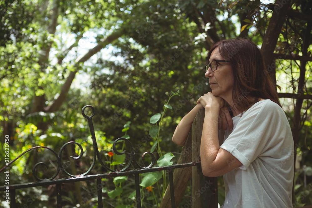 Thoughtful woman leaning on gate in garden Thoughtful woman leaning on gate in garden
