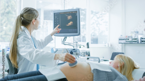 In the Hospital, Obstetrician Uses Transducer for Ultrasound/ Sonogram Screening / Scanning Belly of the Pregnant Woman and Points Finger at Screen. Screen Shows 3D Image of forming Baby. photo