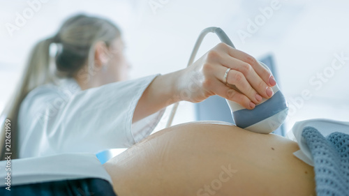 In the Hospital, Low Angle Shot of the Obstetrician Using Transducer for Ultrasound/ Sonogram Screening / Scanning Belly of the Pregnant Woman. Computer Screen Shows 3D Image of Baby.