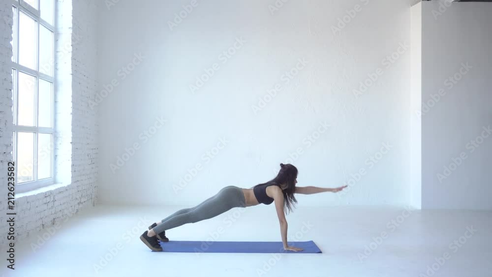 Full-length view of the young sportive trainer standing in plank pose and raising hands up in the white isolated studio. 4k.