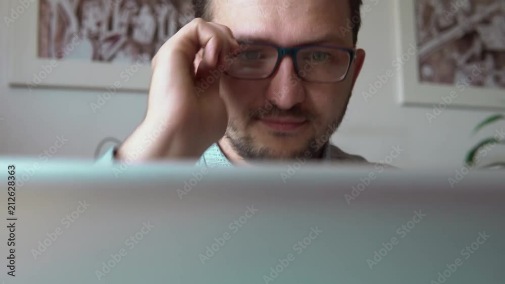 close up. young businessman sitting at the laptop. trying to see the screen but can't see. puts on glasses and looks again close up. young businessman sitting at the laptop. trying to see the screen but can't see. puts on glasses and looks again