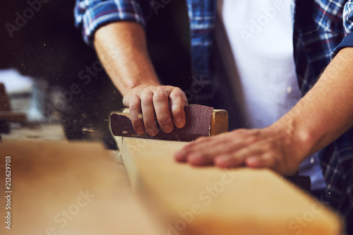 Close-up of carpenter using sandpaper on a wooden plank in a carpentry shop photo