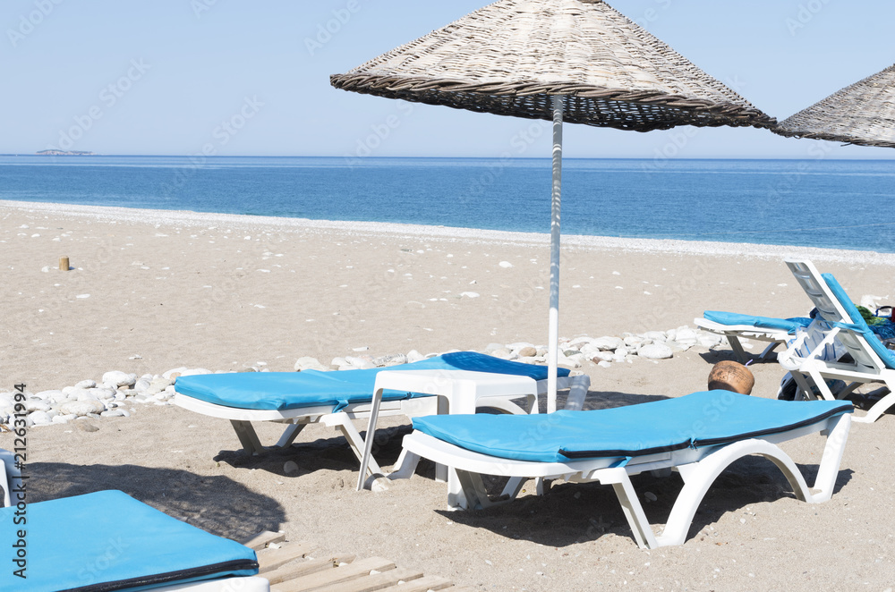 Sunbeds under an umbrella on a sandy beach against blue sea and sky background on bright sunny day