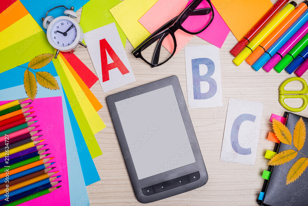 Bright background for your advertising: stationery and an e-book on a wooden desk, top view. Bright background for your advertising: stationery and an e-book on a wooden desk, top view.