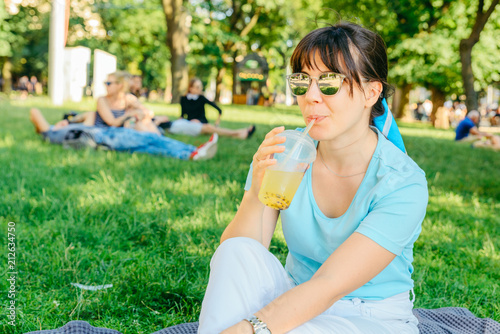 woman holding cool drink in city park. blurred background