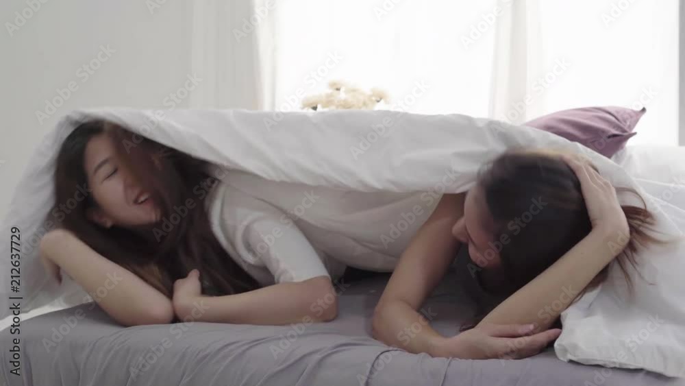 Beautiful young asian women LGBT lesbian happy couple hugging and smiling while lying together in bed under blanket at home. Funny women after wake up. LGBT lesbian couple together indoors concept.