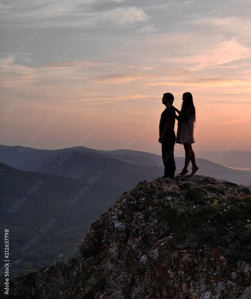 Fototapeta premium A man and a woman stand on top of the mountain at sunset.