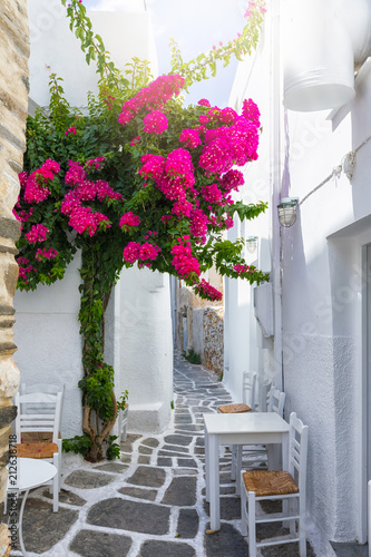 Kleine Gasse auf den Kykladen, Paros, Griechenland, mit weißen Häusern, Tischen und Stühlen und bunten Bougainvillea Blumen