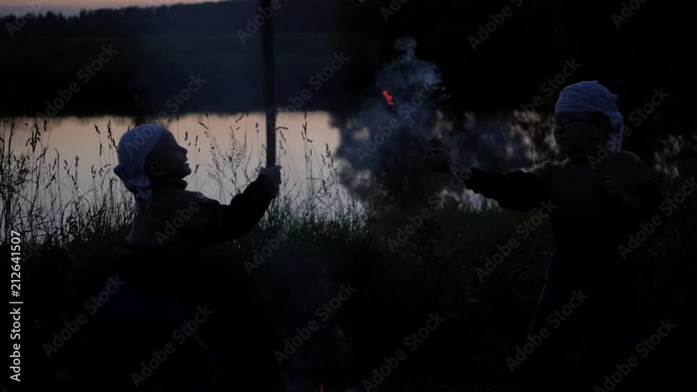 sparks from burning sticks. Battle of children to burning dubankah. children fight against the background of the river. Coals from burning sticks scatter in different directions. Slow motion sparks from burning sticks. Battle of children to burning dubankah. children fight against the background of the river. Coals from burning sticks scatter in different directions. Slow motion