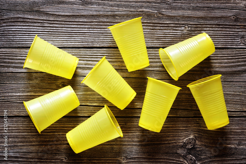 Disposable yellow plastic cups on a wood background