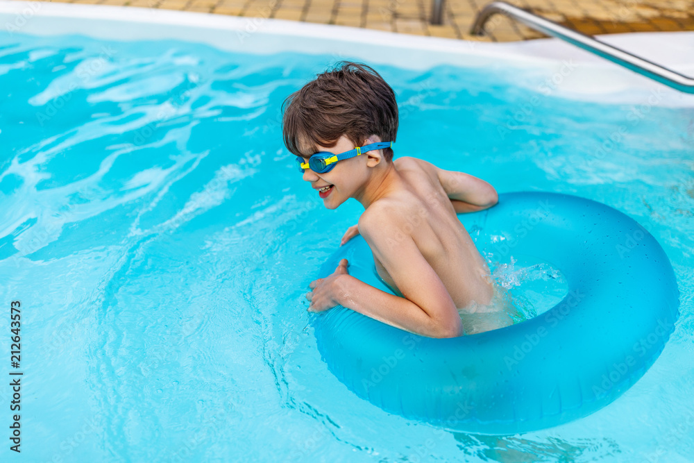 side view of happy boy in swimming glasses with inflatable ring swimming in swimming pool on summer day