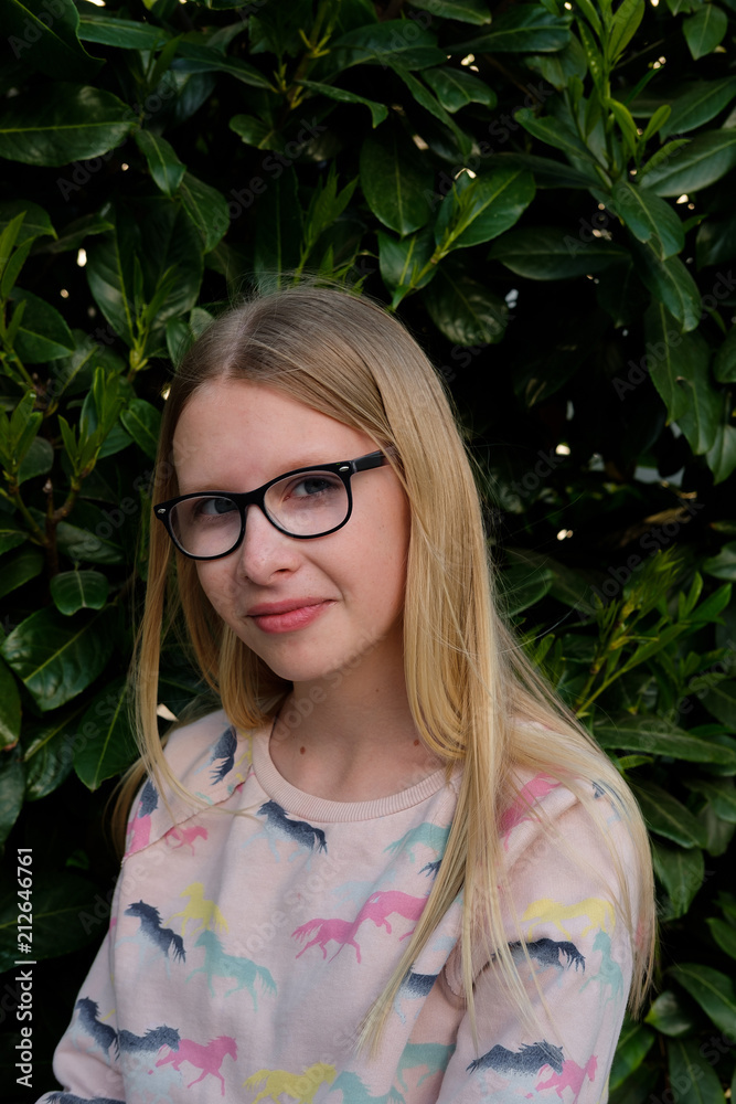 portrait of blond girl in park. teenager girl in eyeglasses outdoors on background of green hedge portrait of blond girl in park. teenager girl in eyeglasses outdoors on background of green hedge