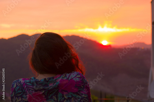 woman stands with her back to the camera at sunset on the balcony overlooking the mountains
