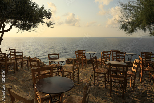 Iron tables and wooden chairs  typical traditional greek cafes  overlooking the roofs of houses and the sea in Monemvasia  Peloponnese  Greece  June 2018.