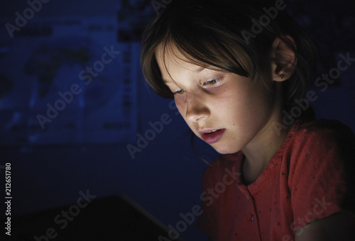 Dolly shot caucasian girl lying in bed playing tablet in social internet in dark blue light under blacket. Childhood, communication and technology concept photo