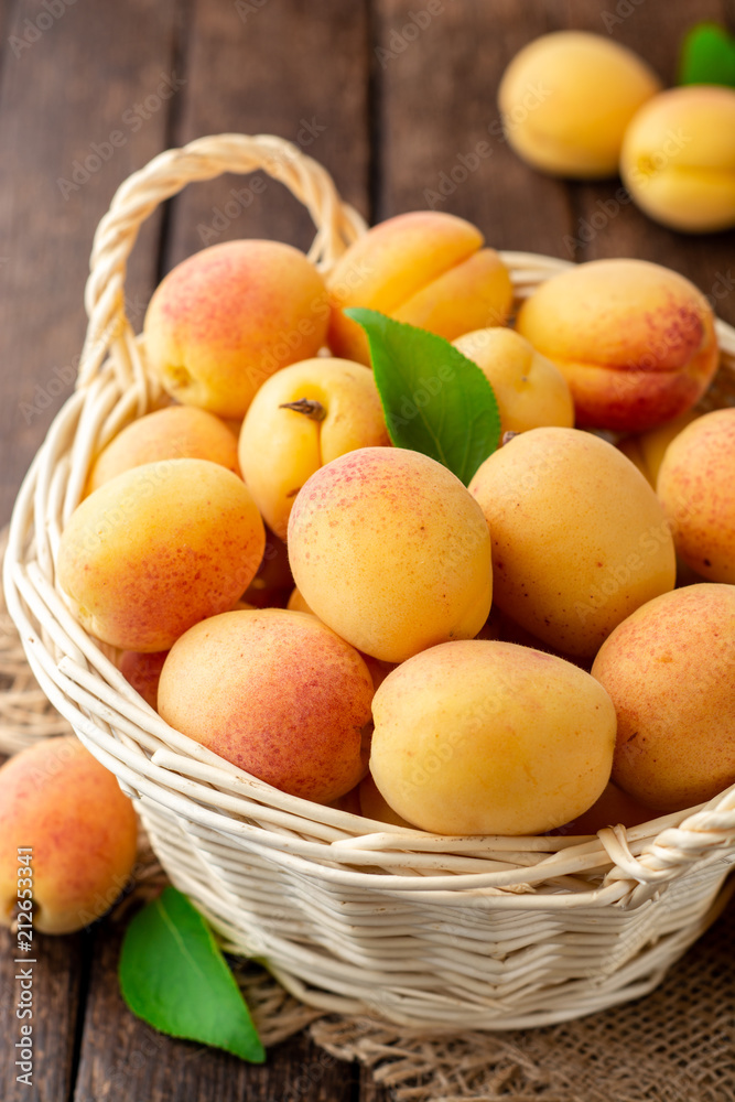 Fresh apricots in wicker basket on dark wooden background Fresh apricots in wicker basket on dark wooden background