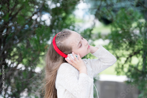 Little girl listen music in summer park. Melody sound and mp3. Child enjoy music in headphones outdoor. Fashion kid and modern technology. Summer vacation and fun