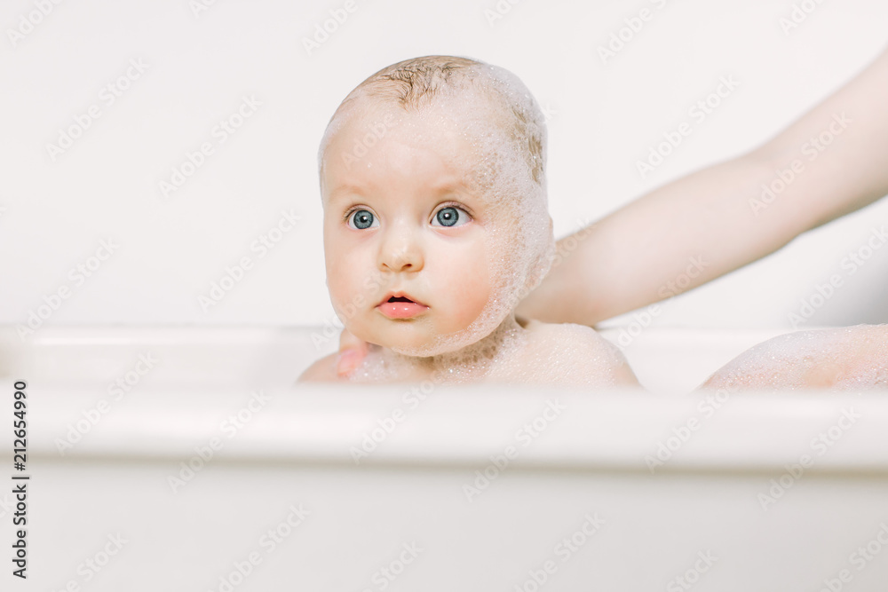Happy laughing baby taking a bath playing with foam bubbles. Little child in a bathtub. Infant washing and bathing. Hygiene and care for young children. Happy laughing baby taking a bath playing with foam bubbles. Little child in a bathtub. Infant washing and bathing. Hygiene and care for young children.