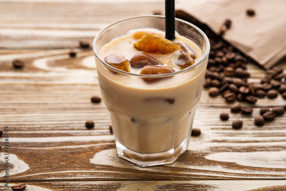 Cold coffee glass with ice cubes on wooden table background. Ice coffee. Copy space.