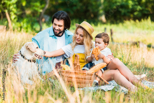 parents and son sitting on blanket at picnic and palming dog