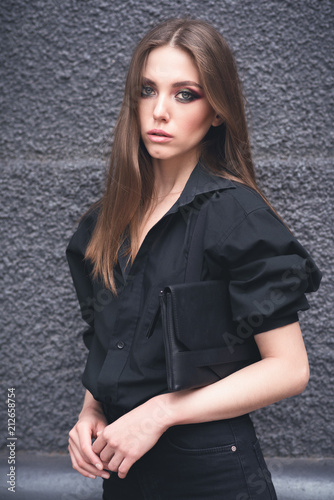 Beautiful girl in black clothes oversize with suspenders. Dark background. Toned image.