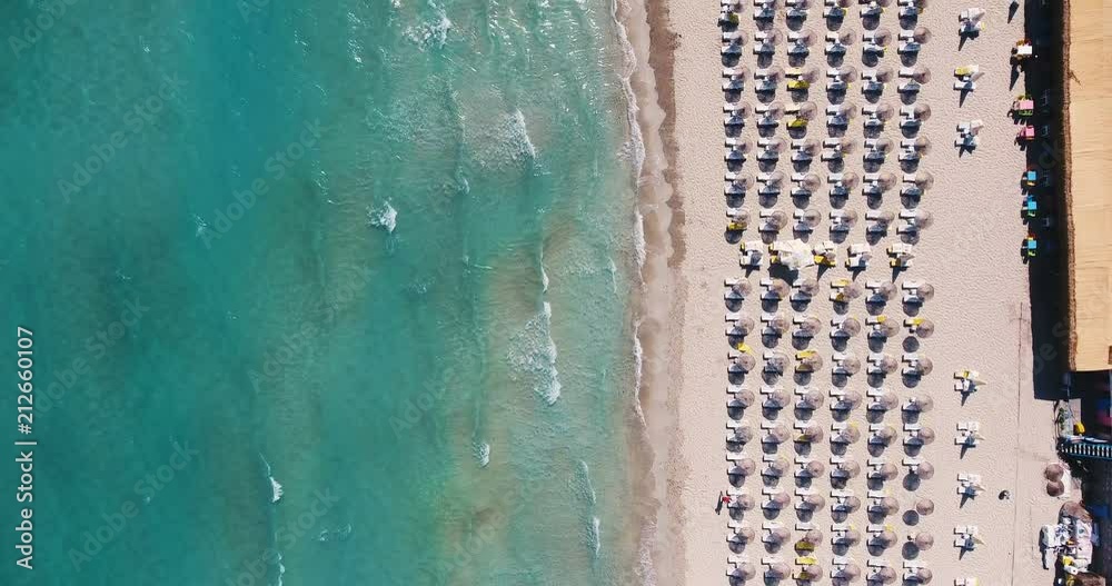 Aerial - Umbrellas on the beach. Top down view of waves hitting sandy shore