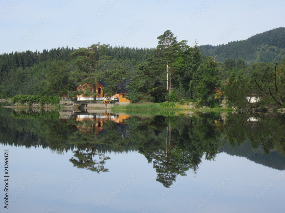 Fototapeta premium SunReflection of house and trees in crystal clear lake water