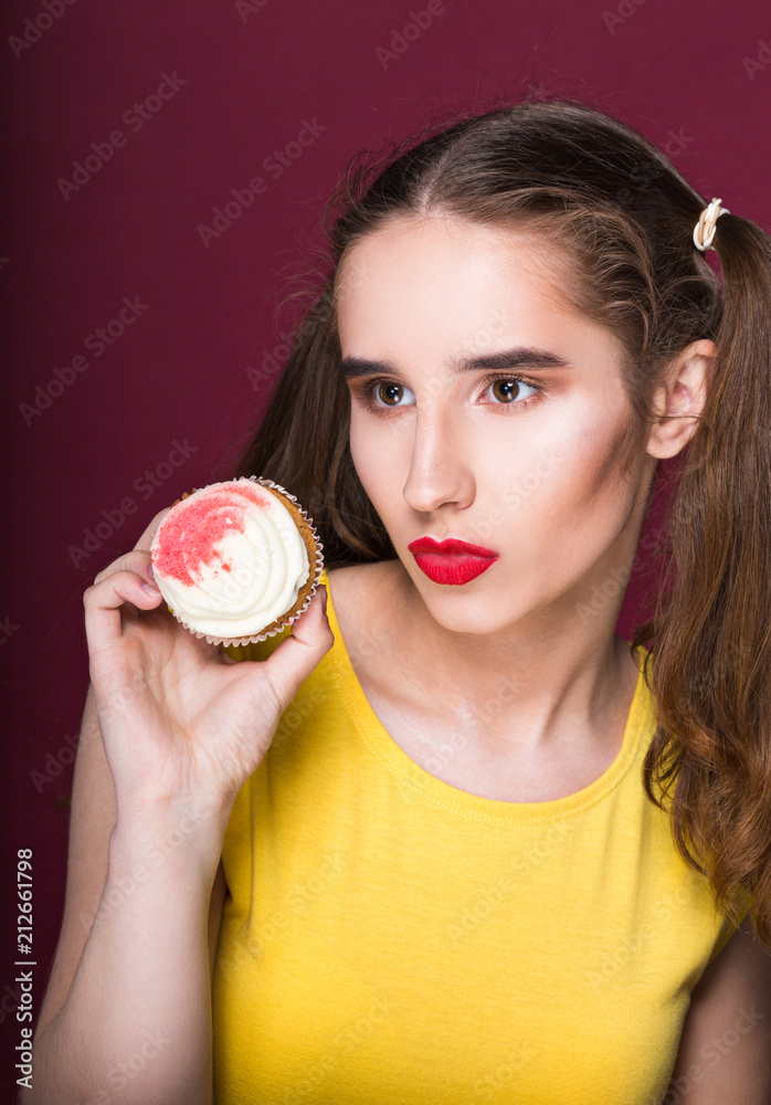 Fashionable brunette girl with bright makeup holding sweet cupcake. Studio shot on a red background Fashionable brunette girl with bright makeup holding sweet cupcake. Studio shot on a red background