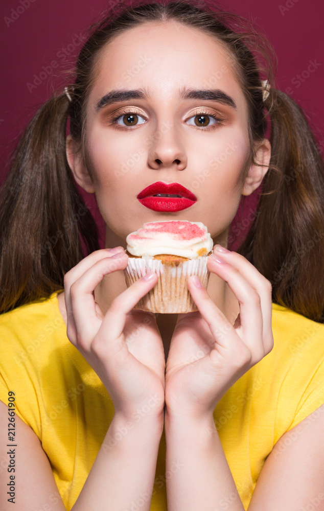 Pretty brunette woman with bright makeup holding sweet cupcake. Studio shot on a red background Pretty brunette woman with bright makeup holding sweet cupcake. Studio shot on a red background