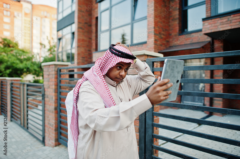 Middle Eastern arab man posed on street against modern building with tablet at hands.