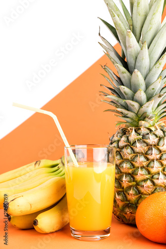 Fresh bananas and pineapple with green leaves. Glass of juice and Tropical Fruits on an orange and white background. Creative concept