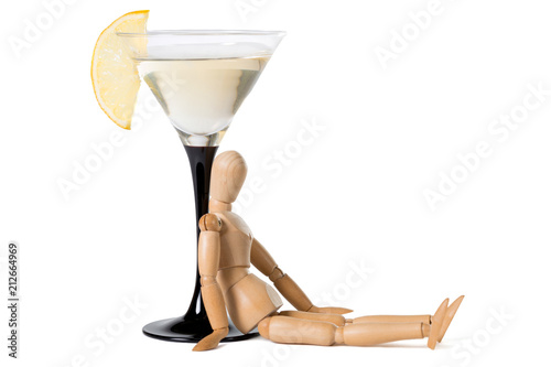 Wooden mannikin sitting near glass of vermouth. Concept of drunkenness, alcohol abuse.