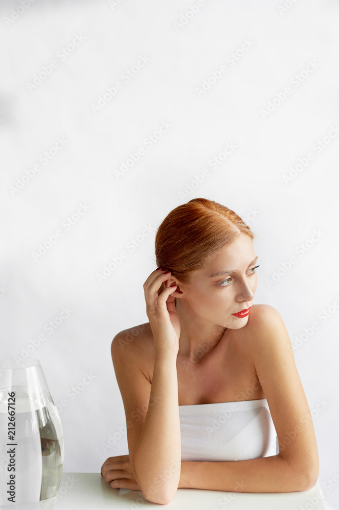 Beautiful girl of European appearance. Red hair with a touch of honey.Beauty shooting. He sits at the white table and looks thoughtfully to the side Beautiful girl of European appearance. Red hair with a touch of honey.Beauty shooting. He sits at the white table and looks thoughtfully to the side