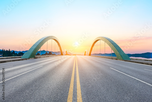 Empty asphalt road and bridge at sunset