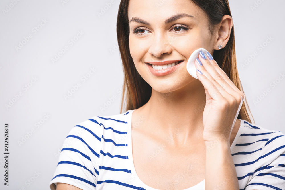 A picture of a happy woman cleaning her face with cotton pads over white background