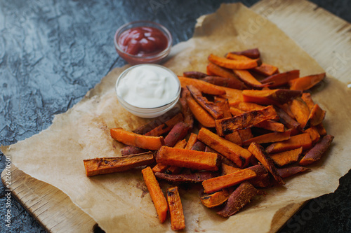 Homemade orange baked sweet potato fries with sour cream sauce and ketchup. Healthy lifestyle, organic food, selective focus
