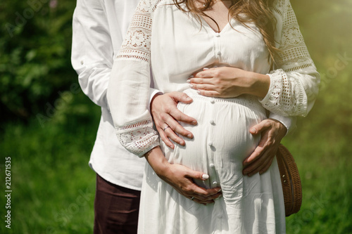 Pregnant couple posing in park in summer day.