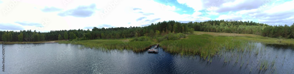Panorama aerial view on mud lake with forest, reed and blue cloud sky horizon
