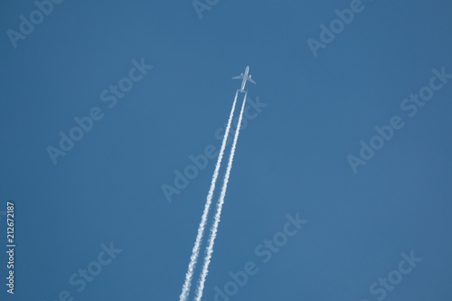Airplane flying at high altitude leaving its white wake over blue sky