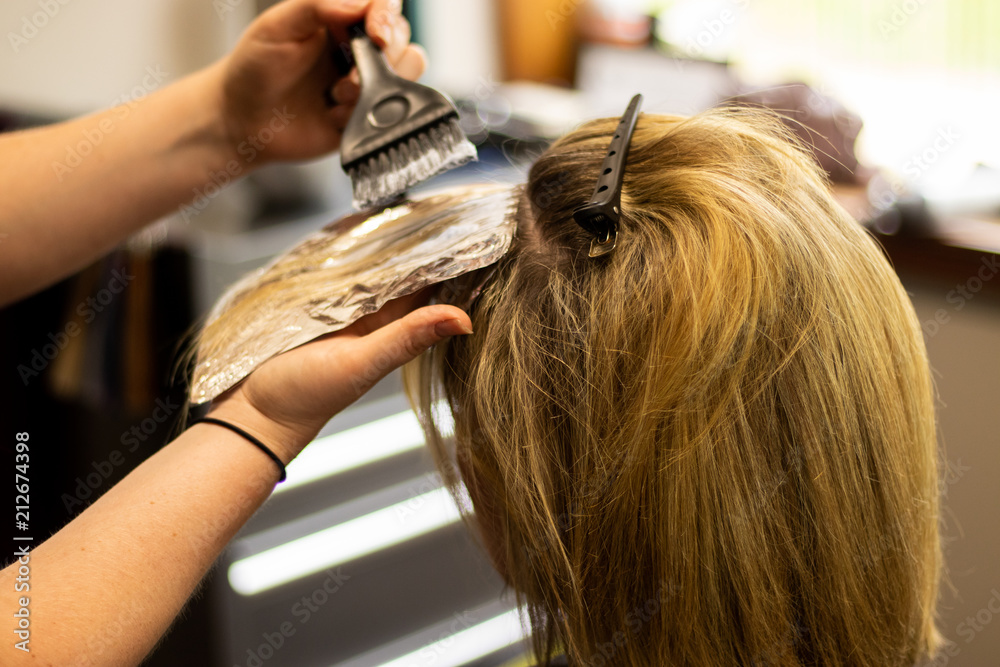 Fototapeta premium Blonde woman receiving haircut at a salon. Woman with blonde highlights. Hair foils on a female client. Master stylist cutting hair