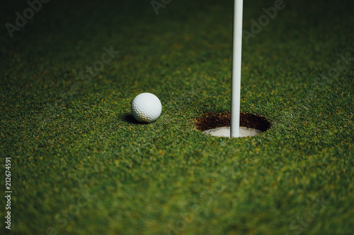 golf ball nearby hole with pin flag, green grass background, closeup view