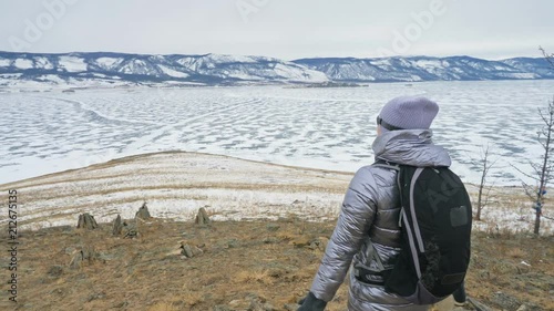 Travel of woman on ice of Lake Baikal. Close unique buddhist stupa burkhan monument symbol mystical historic ritual island Ogoi landscape mountains shamanic worship. Trip to winter island. Hiker wears photo