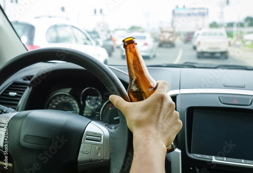 A driver holding alcoholic bottle while driving / Drunk driving concept photo