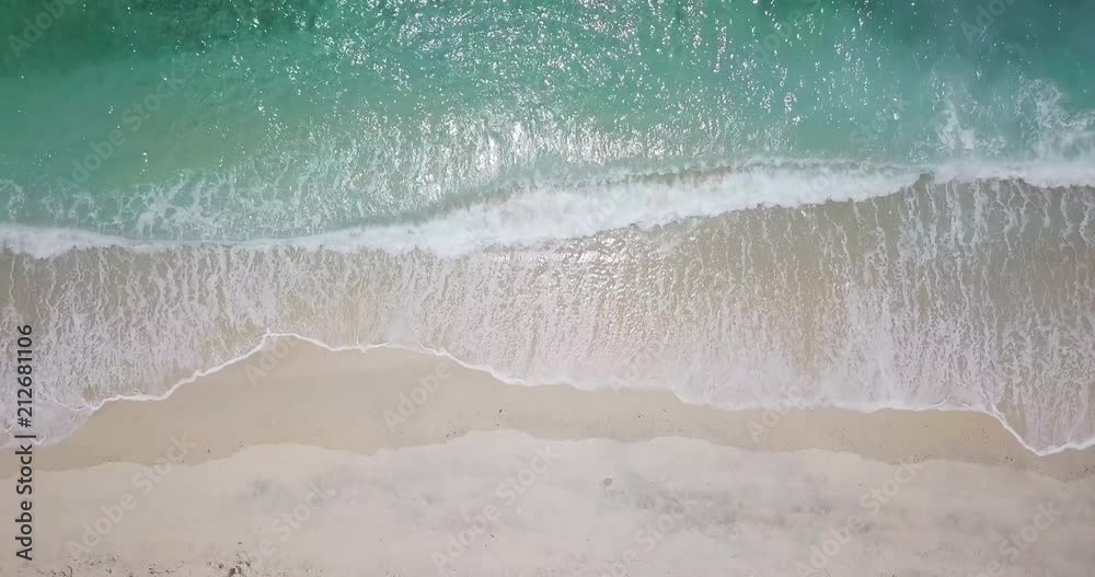 Top camera view over white sand beach and little waves of blue sea or ocean running on the shore. Summer beach background. Sand and sea. Aerial drone slow motion footage Uhd 4K.